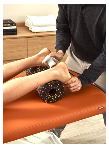 Un physiothérapeute appliquant la thérapie TECAR sur la cheville d'un patient.