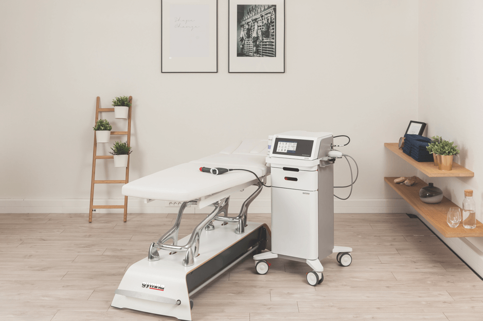 Appareil Gymna ShockMaster placé à côté d'une table de traitement Gymna pour la physiothérapie